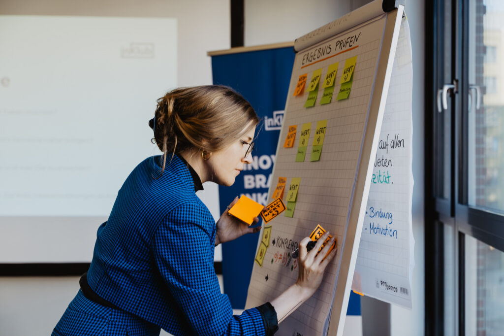 Die Projektleitung des Mentoring Program klebt post-its auf ein Whiteboard