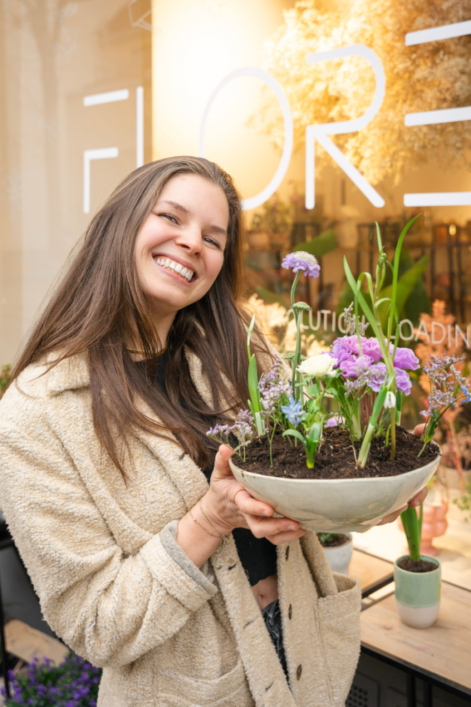 Katharina lächelt mit Blumen in der Hand in die Kamera